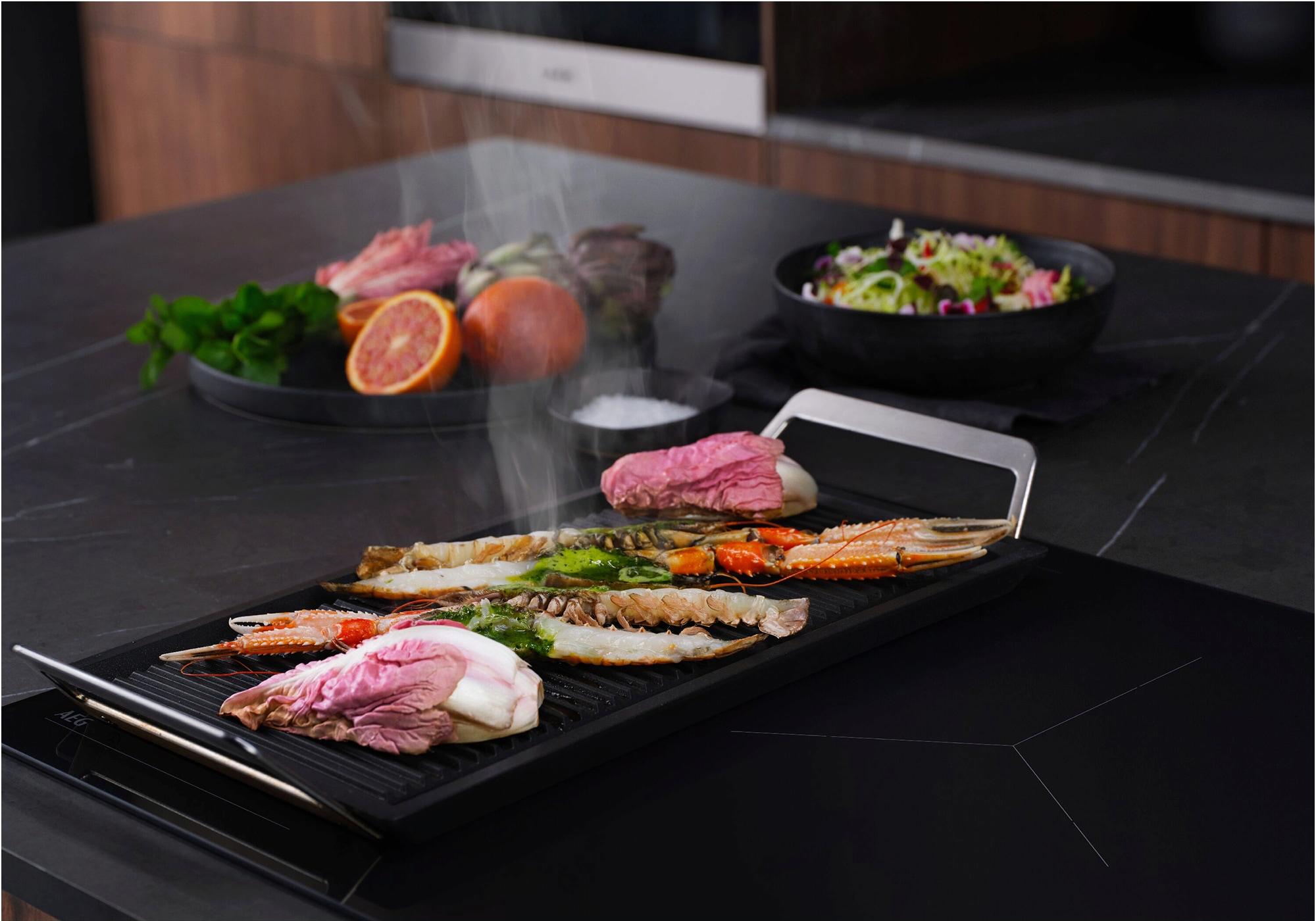 AEG Induktionskochfeld mit Gemüse, Fleisch und Fisch beim Kochen